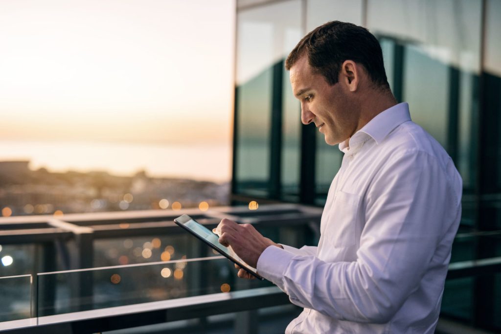 Smiling businessman standing on an office balcony using a tablet